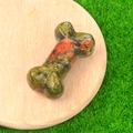 Green and red unakite stone bone carving on wooden tray over green grass background - Unakite