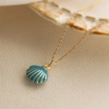 Elegant gold shell pendant necklace with blue enamel drip on a textured beige surface - Blue