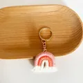 Detailed macro of a handmade woven rainbow keychain with fringes on a wooden tray - Pink Orange