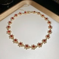 Macro detail of a gold necklace with red floral gems on a white tray with gold edges - Necklace-Gold-Red