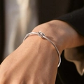 Minimalist silver knot bangle in polished titanium steel worn on wrist over dark cuff - Silver