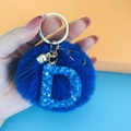 Dettaglio del portachiavi a pompon blu con lettera D glitterata e anello in metallo oro - Lettera D