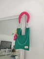 Green knitted handbag with pink padded handle and chunky green chain in a lifestyle setting - Green + Shoulder Strap Set