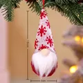 Knitted Christmas gnome ornament with red snowflake hat hanging on a tree branch - Style M