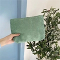 Detail shot of a green corduroy makeup bag held in hand against a blue wall background - Green