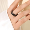 Detail of minimalist matte black stainless steel ring on model hand with elegant lighting - Black