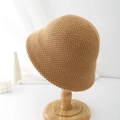 Close-up of khaki knitted bucket hat showing premium thick stitch texture on a wooden stand - Camel