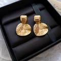 Detailed shot of golden square and hammered round earrings set in a black jewelry box - Gold