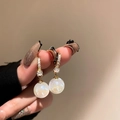 Elegante goldene Ohrringe mit glänzenden Strasssteinen und weißen Perlen in der Hand - Strass Perlen Anhänger Stil / Gold