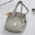 Detail of grey-green pleated tote bag with drawstring closure on minimalist background - Gray