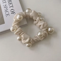 Close-up of elegant cream satin scrunchie featuring large glossy pearls on fabric folds - Cream
