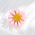 Detailed view of a pink daisy brooch with yellow pistil on white wavy texture background - Pink Daisy