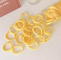 Detalle de gomas de pelo amarillas elásticas con bote transparente en un escritorio - Serie Amarilla