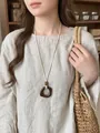Vue détaillée d'un collier ethnique en résine porté avec un haut en lin et un sac en paille - Collier-Blanc-Café