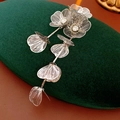 Detail van zilveren bloemspeld met kristalinleg en lange metalen kwastjes op fluweel - Bloem Kwastje Stijl / Zilver