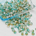 Macro detail of round teal and gold crackle glass beads on white fabric - 8mm / Dawn Color