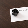 Close-up of a small black floral hair claw clip on a stylish decorative card background - Black