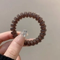 Brown spiral hair tie with transparent resin finish shown in a hand-held close-up view - Single Piece / Jelly Coffee