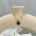 Detail of a gold Figaro chain necklace with a round green gemstone on a beige vase - Necklace / Gold and Deep Green