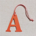 Macro detail of orange pebble grain leather letter A charm on a grey linen background - Letter A Orange