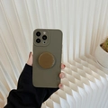 Green silicone iPhone case with brown round pop socket holder shown in a lifestyle shot - 15 Plus / Mud Grey