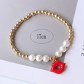 Detail of a 17cm stretch bracelet with gold beads, pearls, and a red lip pendant charm - Style 6 (Lips)