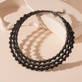 Vue rapprochée du collier choker noir à 3 rangs sur un présentoir géométrique - Ras du Cou Multicouche en Strass Noir Fusil
