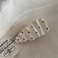 Detail einer cremefarbenen gewellten Haarspange mit schwarzen Punkten auf Stein - Cremeweiße Träne