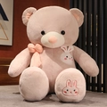 Dettaglio di un orsetto di peluche con fiocco rosa e ricamo di coniglio su tessuto morbido - Beige / 80 cm / 1,1 kg