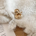 Gros plan d'une broche cheval à bascule dorée épinglée sur un pull en maille beige - Cheval à bascule doré