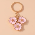 Vue détaillée des breloques fleurs en émail rose sur un porte-clés en métal doré - Rose