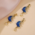 Tre mezzelune dorate con resina blu e stelle in zircone su sfondo in tessuto beige - Blu scuro
