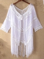 Detailed close-up of white crochet beach cover-up with bohemian tassel hem on wooden hanger - One Size / Tops / White