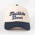 Close-up of Mustache Lover cursive embroidery on beige and navy baseball cap - One Size / Cream/Navy Blue