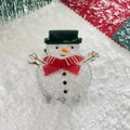 Close-up of glitter snowman hair claw clip with green hat and red bow for Christmas - Snowman