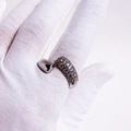 Close-up of open ring with dense dark gemstones held by a hand in a white glove - Adjustable Open / White Gold