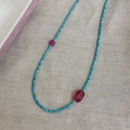 Collana di perline con pietre turchesi e gemme magenta su sfondo di lino naturale - Blu/Rosa
