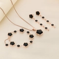 Detail view of a rose gold jewelry set with black clover charms and elegant tassels - Long Tassel 3-Piece Set / Rose Gold