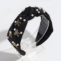 Macro detail of black fabric headband with faux pearls and golden bow accents - Black