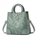 Detailed view of sage green handbag with embossed floral patterns and metal ring handle. - Green