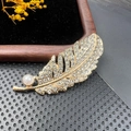 Detailed close-up of a golden feather brooch with pavé rhinestones and a pearl on velvet - BZ017 Feather Shape