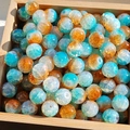Detailed close-up of blue and green glass beads with gold foil on a wooden tray - 10mm / Orange Blue