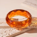 Detailed close-up of geometric faceted amber resin bangle on textured stone - Dark Coffee