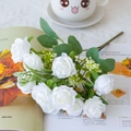 Detail of white artificial silk roses bouquet with green leaves on a cozy desk setting - White