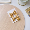 Pair of yellow satin bow hair clips for girls displayed on a white card over a wood tray - Ginger Yellow Bow 2-Piece Set
