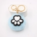 Close-up of light blue plush pom-pom keychain with black and white cat paw leather detail - Cat Claw Gold Keychain / Light Blue