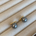 Elegante graue Perlenohrstecker mit goldenem Metallsockel auf beigem Schmucktablett - Gold Grau Glanzperle
