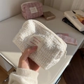 Nahaufnahme einer cremefarbenen Tweed-Kosmetiktasche mit rotem Textetikett und Reißverschluss - Weiß