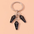 Dettaglio portachiavi gotico con bare nere e croci argentate su sfondo arancione chiaro - Nero Argento