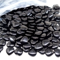 Close-up of small black heart-shaped natural stones spilling out from a clear bag - Black Stone
